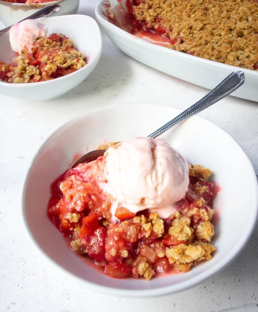 The Ultimate Strawberry Rhubarb Crumble (Sweet, Tart & Easy!) 3 A warm serving of Strawberry Rhubarb Crumble in a bowl, topped with a scoop of melting vanilla ice cream, showing the juicy fruit and crisp topping.
